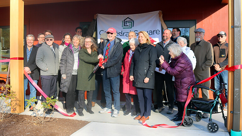 Flanked by state and local officials, funders, residents and others, Cindy Reid of Cathedral Square shares ribbon-cutting duties with Robin Way, former executive director of C.I.D.E.R., during opening ceremonies Nov. 14 for Bayview Crossing.